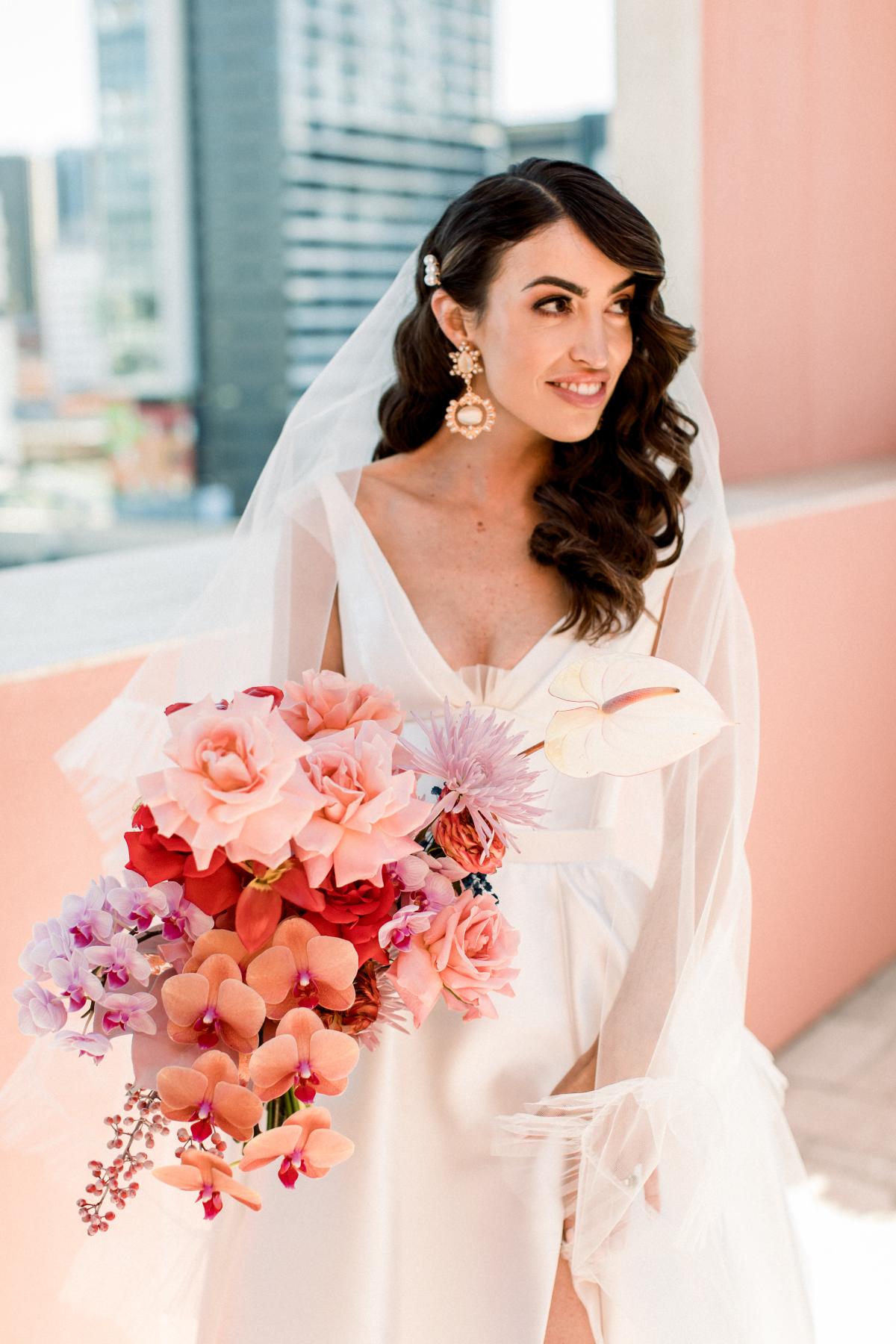 KWH real bride Josey standing in her Taryn Camille gown, a timeless aline wedding dress with long train. She also holds her colourful bridal bouquet.