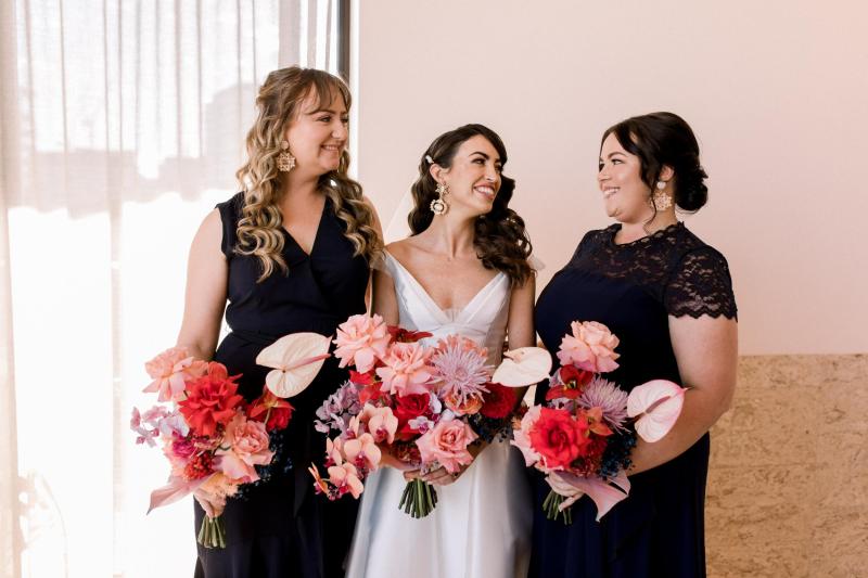KWH real bride Josey standing with her bridesmaids. She wears the timeless Taryn Camille gown, a modern aline wedding dress with high leg split.