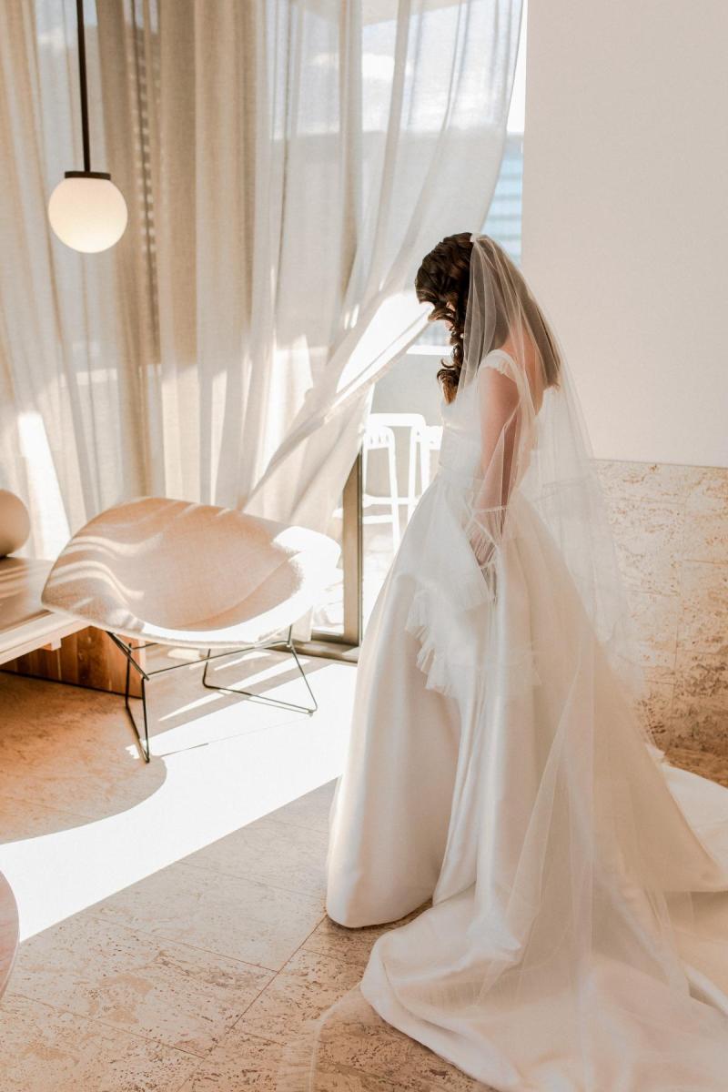 KWH real bride Josey standing in her bridal suite at The Calile hotel in her grand Taryn Camille gown, a modern aline wedding dress with custom cap sleeves.