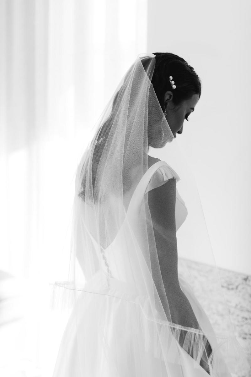 B&W image of KWH real bride Josey standing in her Taryn Camille gown paired with a long veil. Taryn Camille is a modern aline wedding dress with U-shaped neckline.