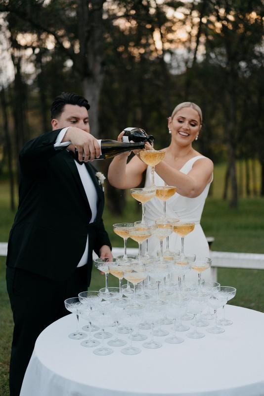 Nikki-Karen Willis Holmes-Eloise & Peter- Keegan Cronin Photography- Bride and groom celebrating their marriage with a timeless champagne tower, surrounded by off white features and classic elements