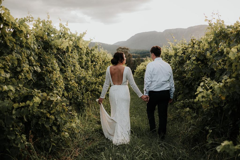 Margareta-Karen Willis Holmes-Victoria & Will- Bride and groom seen holding hands, surrounded by endless vineyards after their ceremony to capture the most beautfiul wedding portraits.