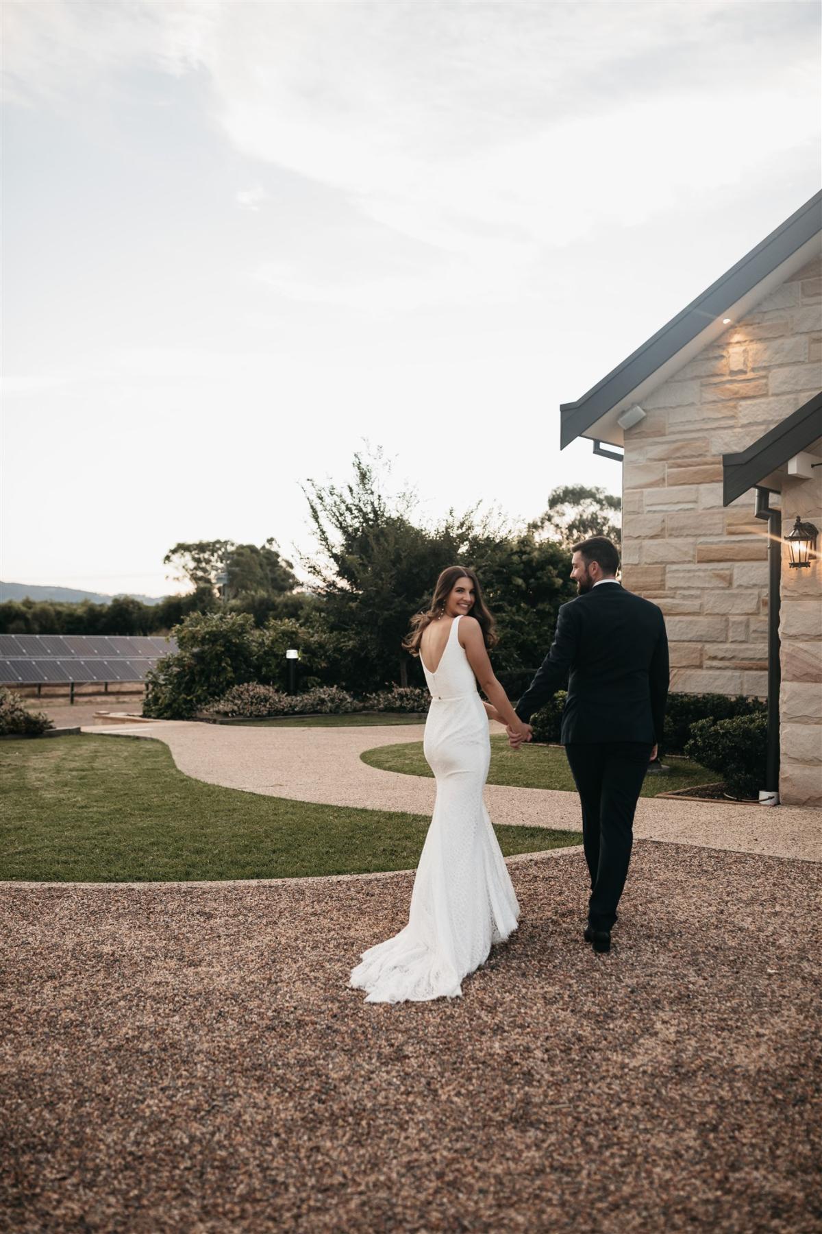 Lorissa & Recce-Rylie-WILD HEARTS collection - Bride and groom seen holding hands, while bride looks gorgeous in our Rylie Gown