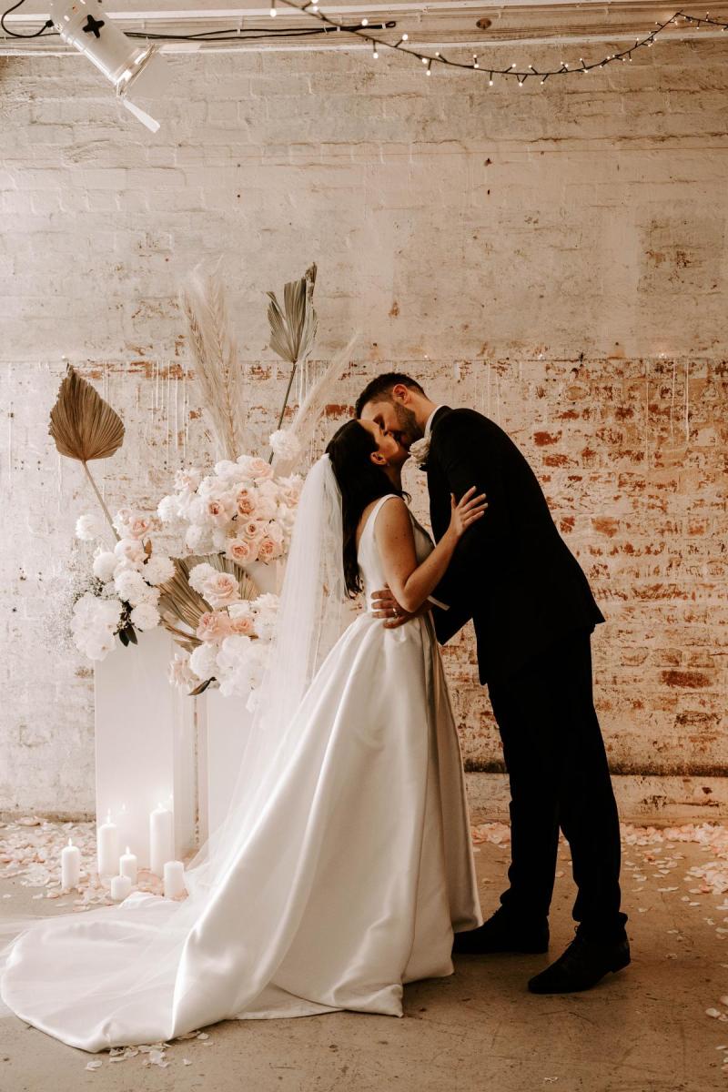 KWH real bride Shenea walking into her venue with her bouquet. She wears the Taryn Camille gown with scoop back and pockiets.