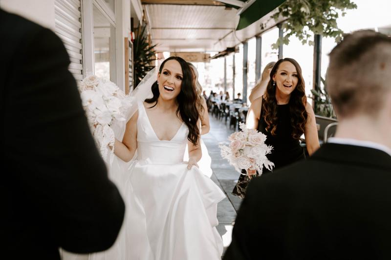 KWH real bride Shenea standing in front of her bridesmaids who wear black. She wears the ivory timeless Taryn Camille gown.