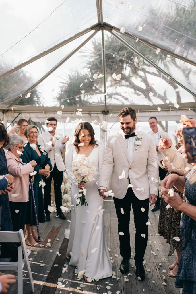 Aubrey - Karen Willis Holmes - Jemma & Brenton - Bride and Groom seen together after their ceramony, celebrating their love with florals thrown in the air with their guests.