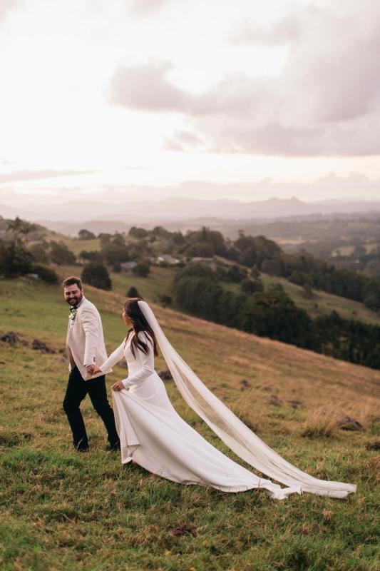 Aubrey - Karen Willis Holmes - Jemma & Brenton - Bride and groom on the mountains for their couple portraits. Brides veil is following the train of her gown to create a dramatic look.