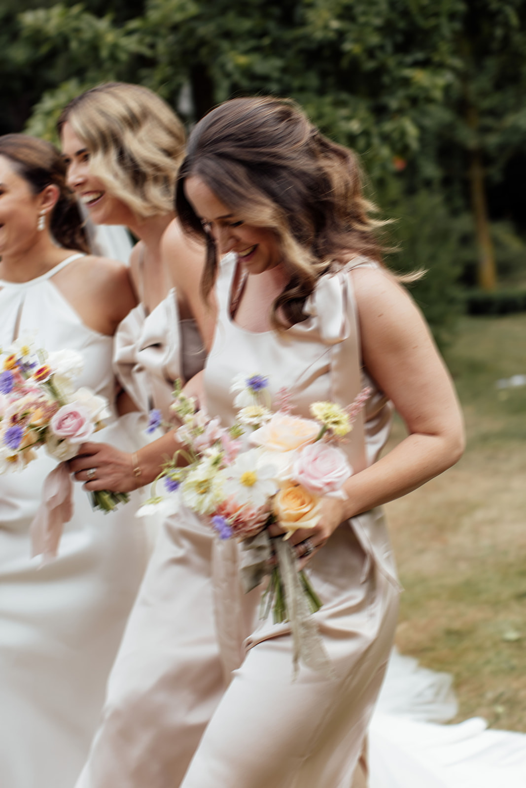 Layne by Karen Willis Holmes-halter neckline wedding dress-Jessica & Tim- Bride is seen running around the garden of her New Zealand Wedding venue with her bridesmaids. Bride and bridesmaids are holding wild floral bouquets, featuring soft pinks and pastel blues.