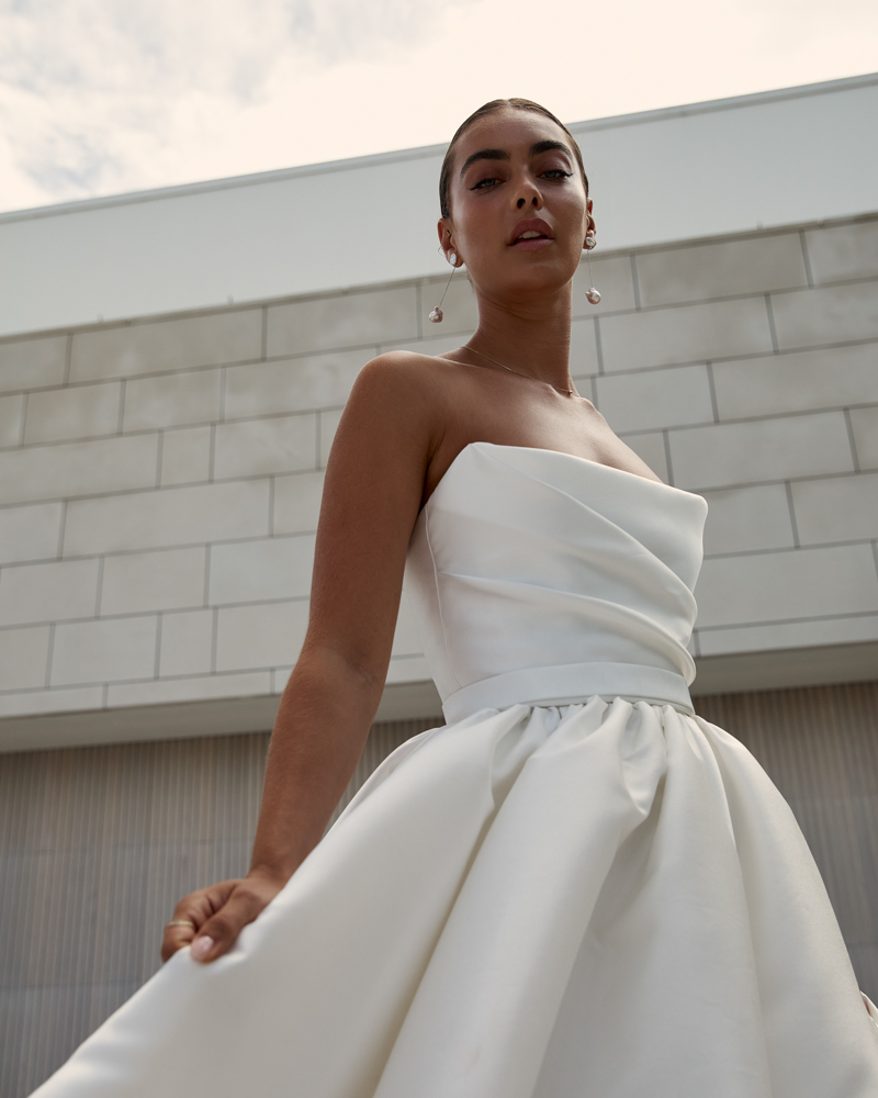 Cropped in image of Lou Lou Sabrina is a classic Wedding dress with a draped corset bodice featuring a full, pleated skirt, modern side split and pockets by Karen Willis Holmes 2023 Bridal Campaign.