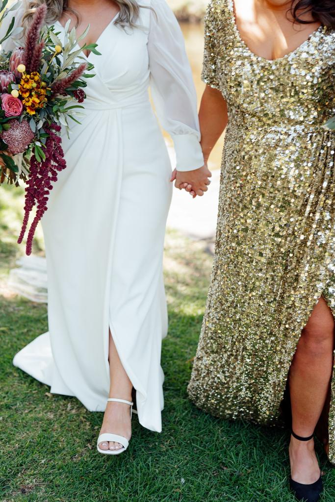 Nikki - Karen Willis Holmes - Sarah & Gabriella- LGBT wedding. Same sex couple are holding hands while they walk down the aisle, holding a colorful floral arrangement. Bride is wearing the Nikki gown from Karen Willis Holmes Bridal.