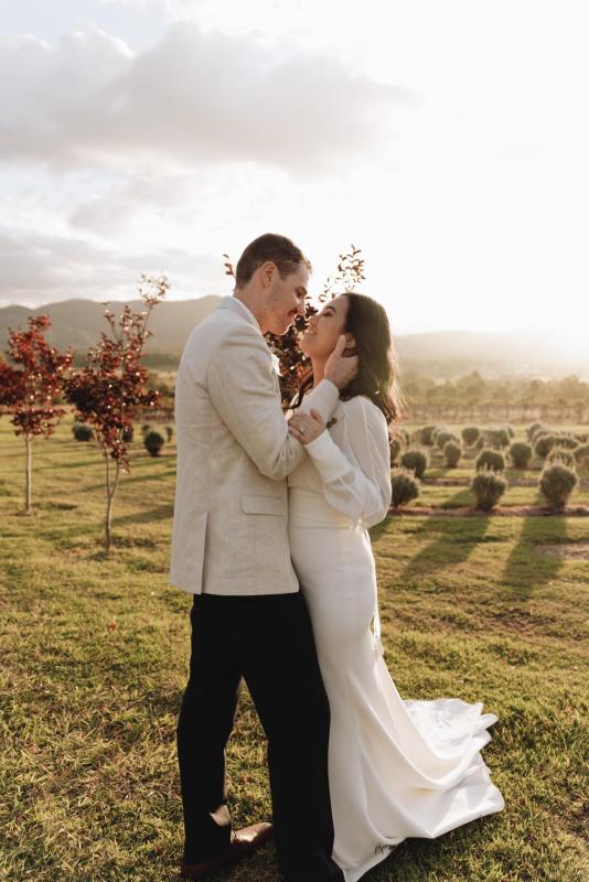 The Brie wedding dress by Karen Willis Holmes Bridal is a statement long sleeve sheer high neck gown with a low back, fitted skirt with a split. Brie features a v neck spaghetti strap bodice under the dreamy cuffed sleeves.