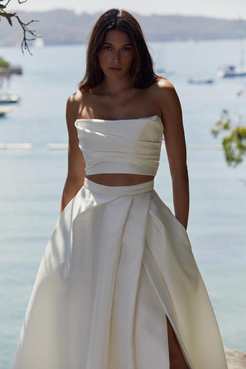 Lou Lou bralette and Gianna skirt is a sexy modern wedding gown. Lou Lou bralette is a strapless draped crop bodice and is paired with the Gianna skirt which also features a modern drape style, pockets and a statement split.