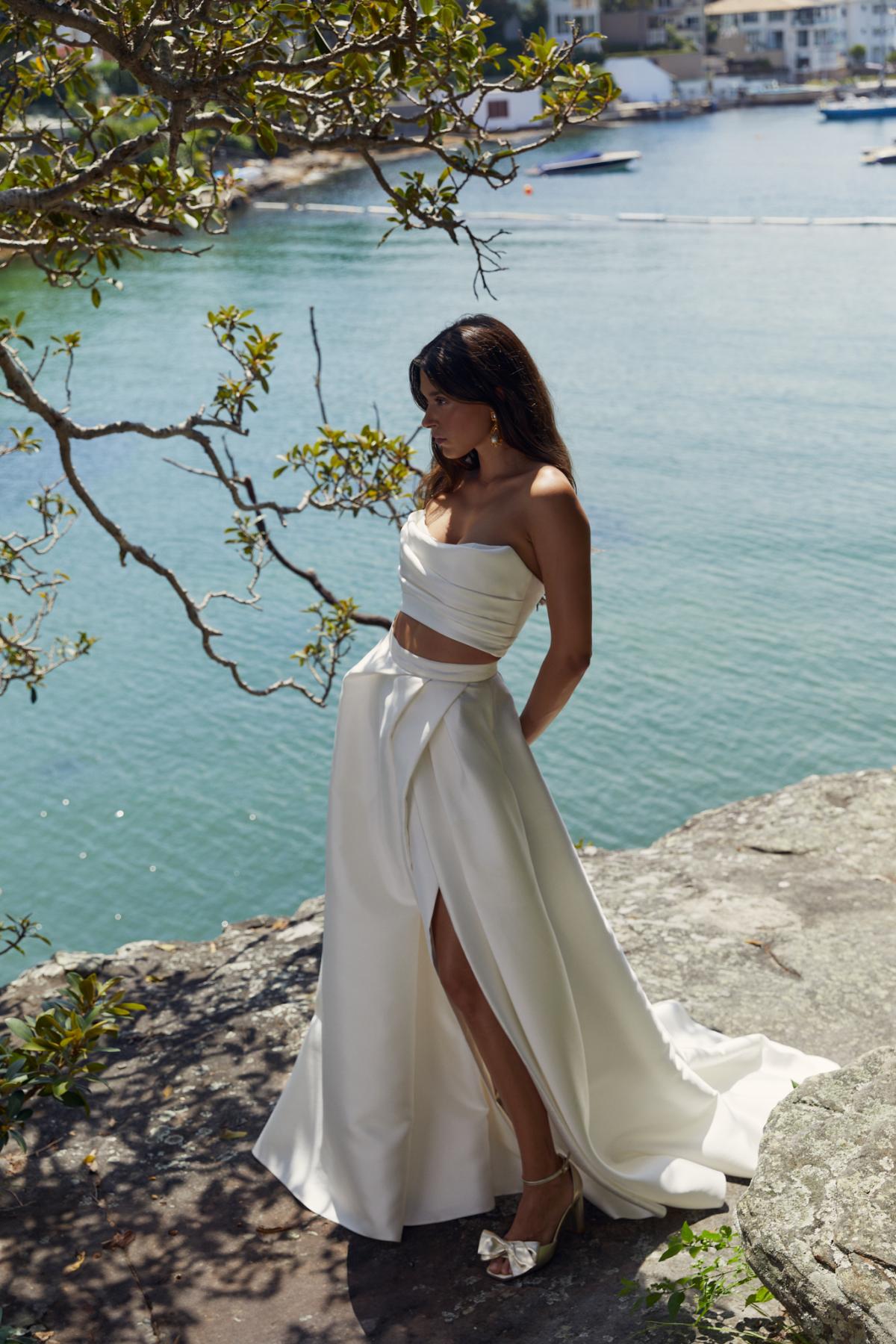 Lou Lou bralette and Gianna skirt is a sexy modern wedding gown. Lou Lou bralette is a strapless draped crop bodice and is paired with the Gianna skirt which also features a modern drape style, pockets and a statement split.