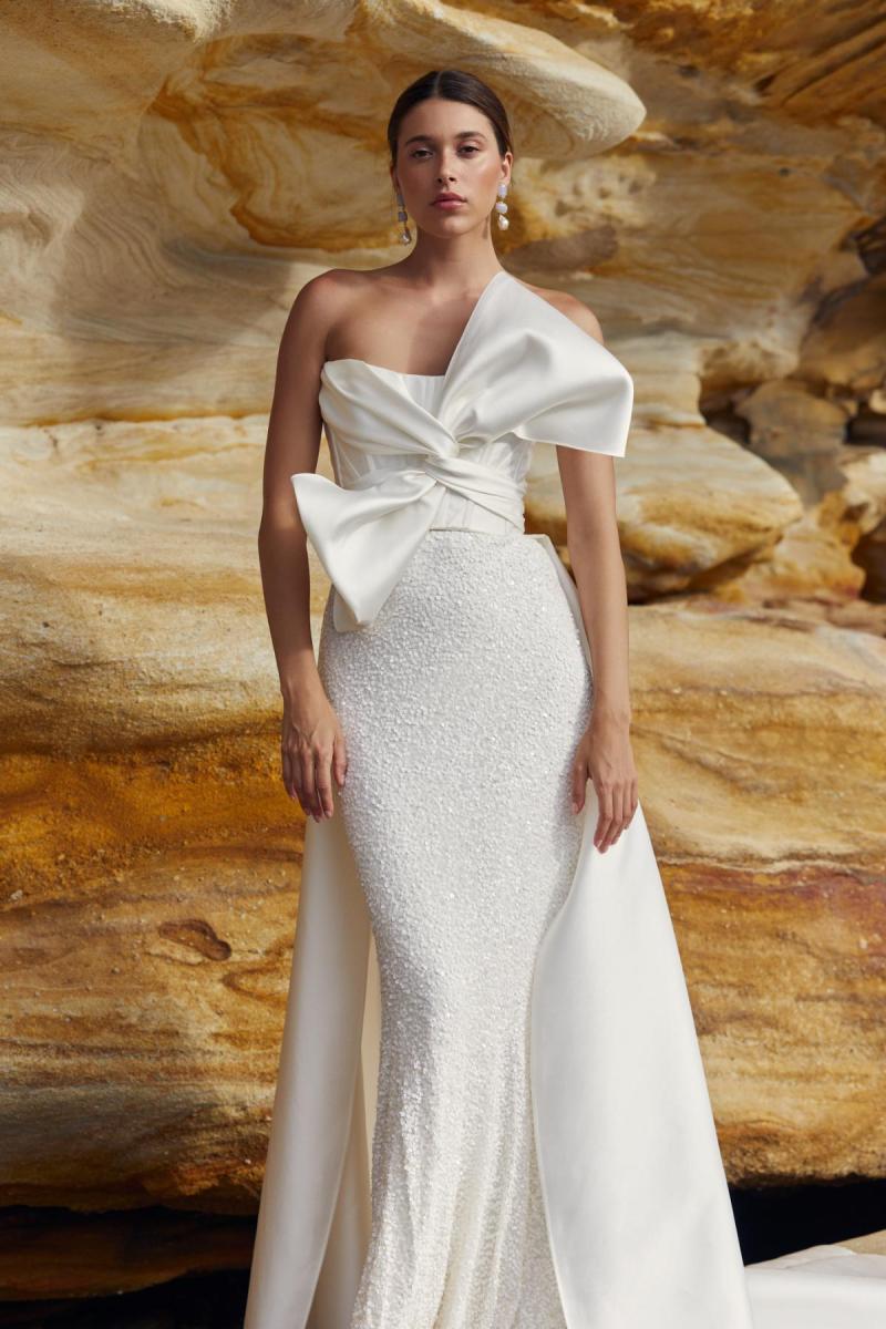 Ines & Avery is a modern statement wedding dress. Featuring a statement Bow on the bodice, paired with a beaded column shaped skirt and our detachable lindy train.