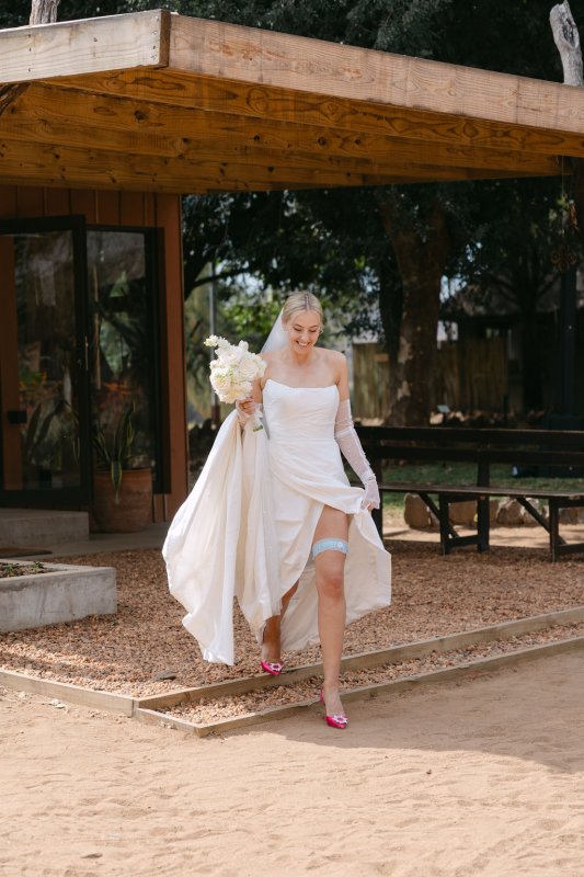 Bride walking towards the ceremony, fully dressed in our Emma Gown, Erin's gloves and Pearl Graded veil.